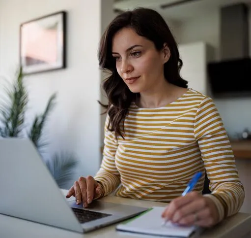Young woman sitting at her dining room table searching for affordable health insurance on her laptop