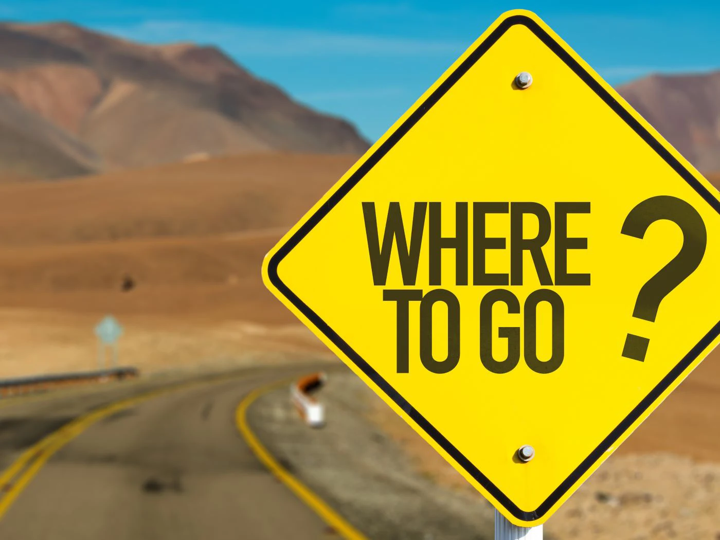 A road sign reading “Where To Go?” on an empty desert road.