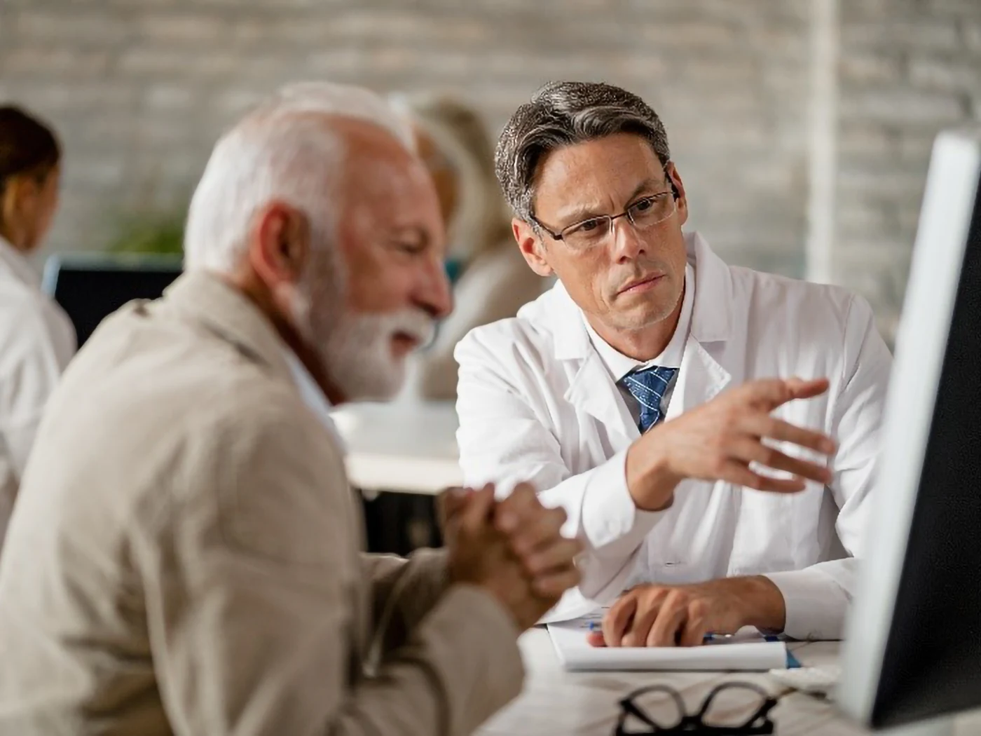 A doctor in a white lab coat consults with a patient at a computer in a medical office.