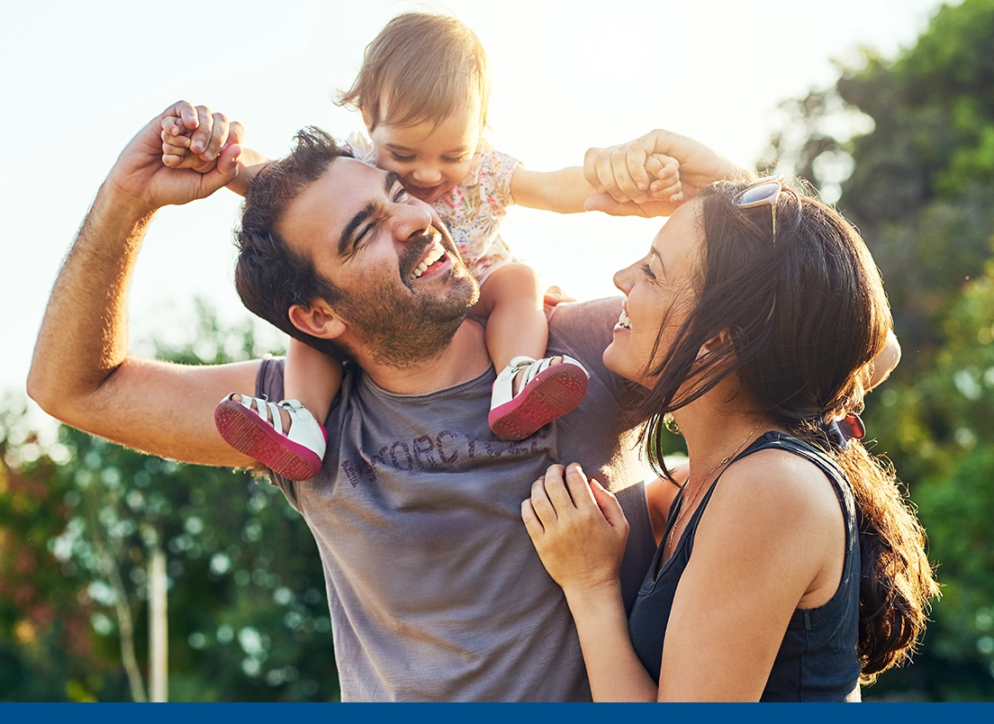 young father with toddler on his shoulders and mother standing by in the sunshine