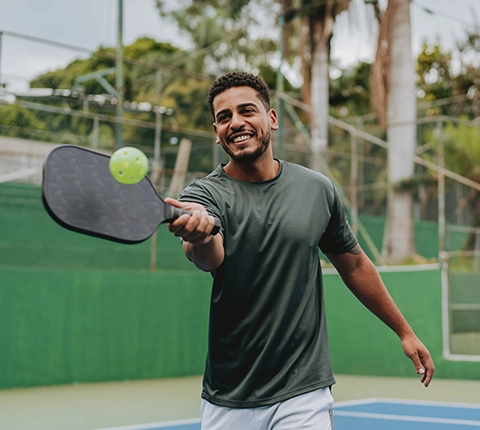 Hombre joven y saludable sonriendo mientras juega pickleball en la cancha