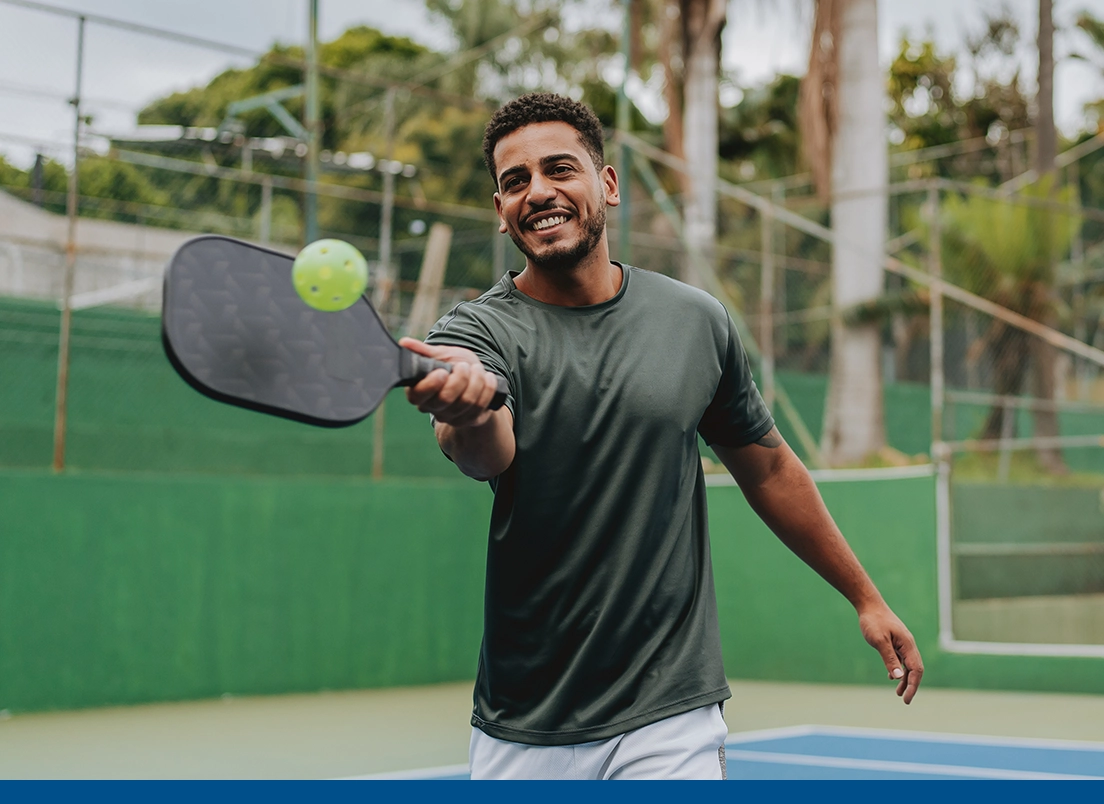 Hombre joven y saludable sonriendo mientras juega pickleball en la cancha