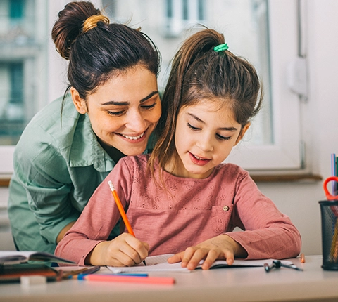 woman happily helping her young daughter with her homework