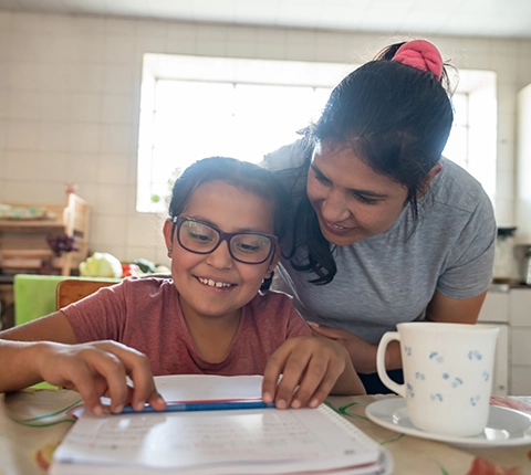 Mujer ayudando felizmente a su hija pequeña con sus tareas escolares