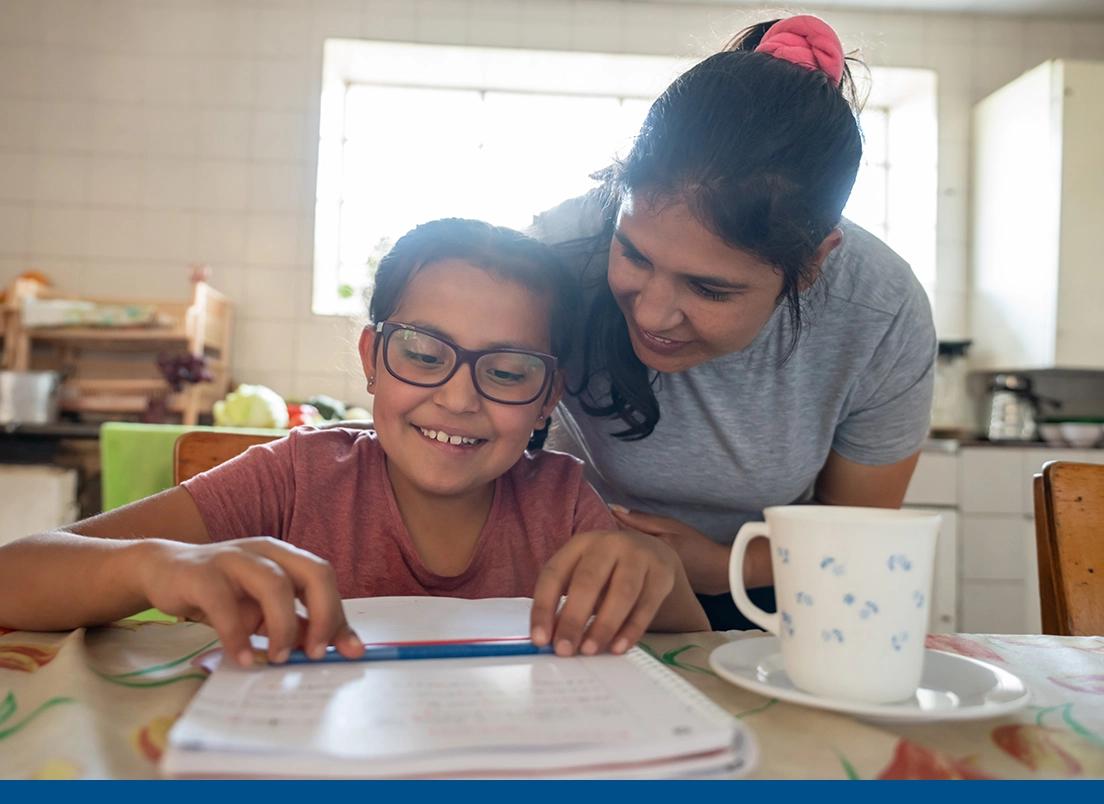 Mujer ayudando felizmente a su hija pequeña con sus tareas escolares