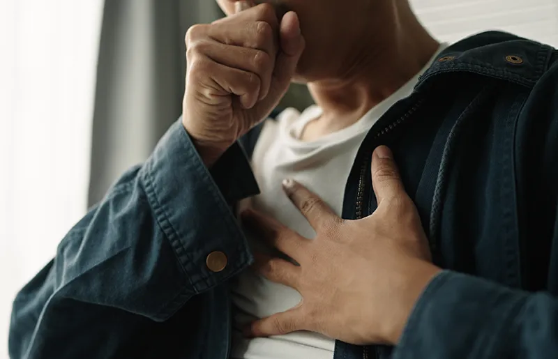 person holding their chest with one hand while coughing into their other