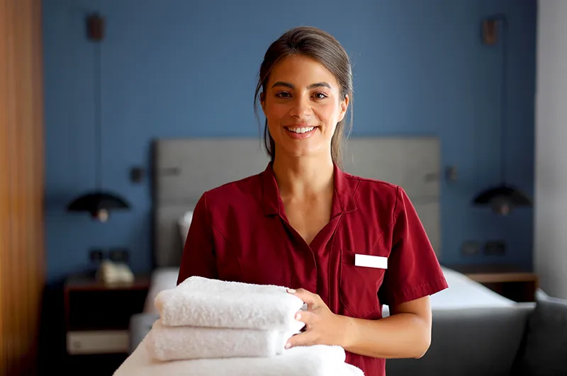 female hotel housekeeper holding towels and smiling at camera