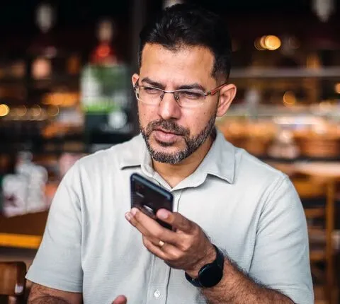 Padre joven sosteniendo a su bebé en brazos mientras habla por teléfono con un agente dedicado sobre la inscripción en un plan de salud de Florida Blue para 2026