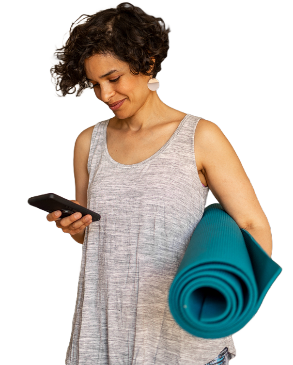 woman on her phone with a yoga mat under one arm