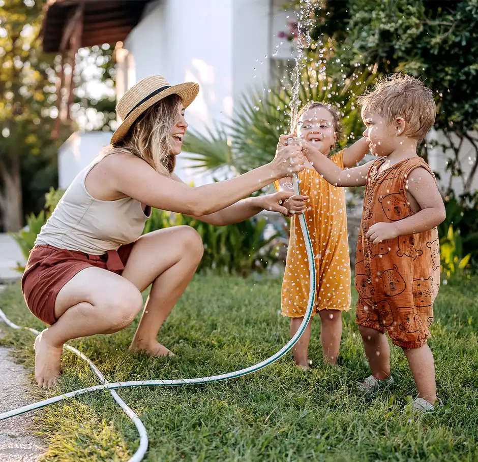 young mother with toddlers playing with hose outside on a hot day