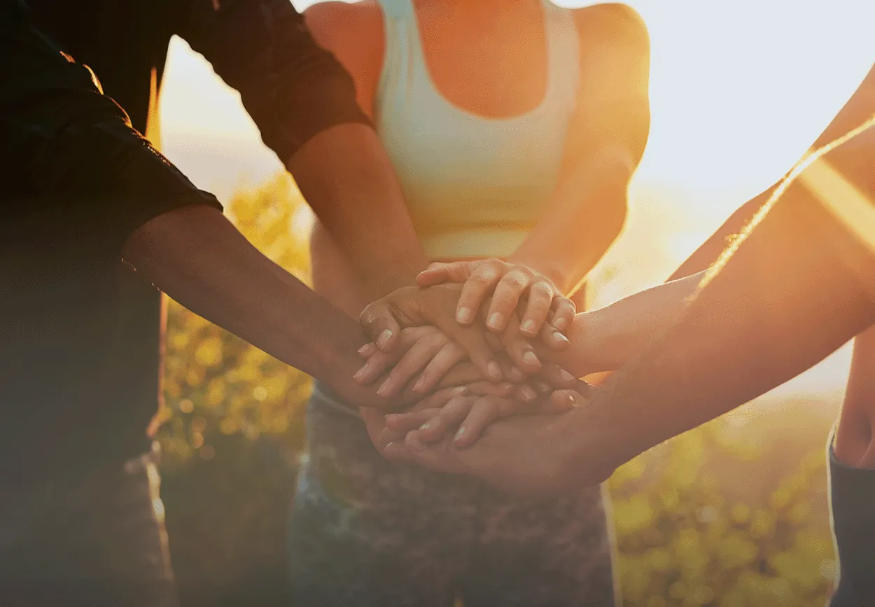 three people putting their hands together, one hand after the other in a field