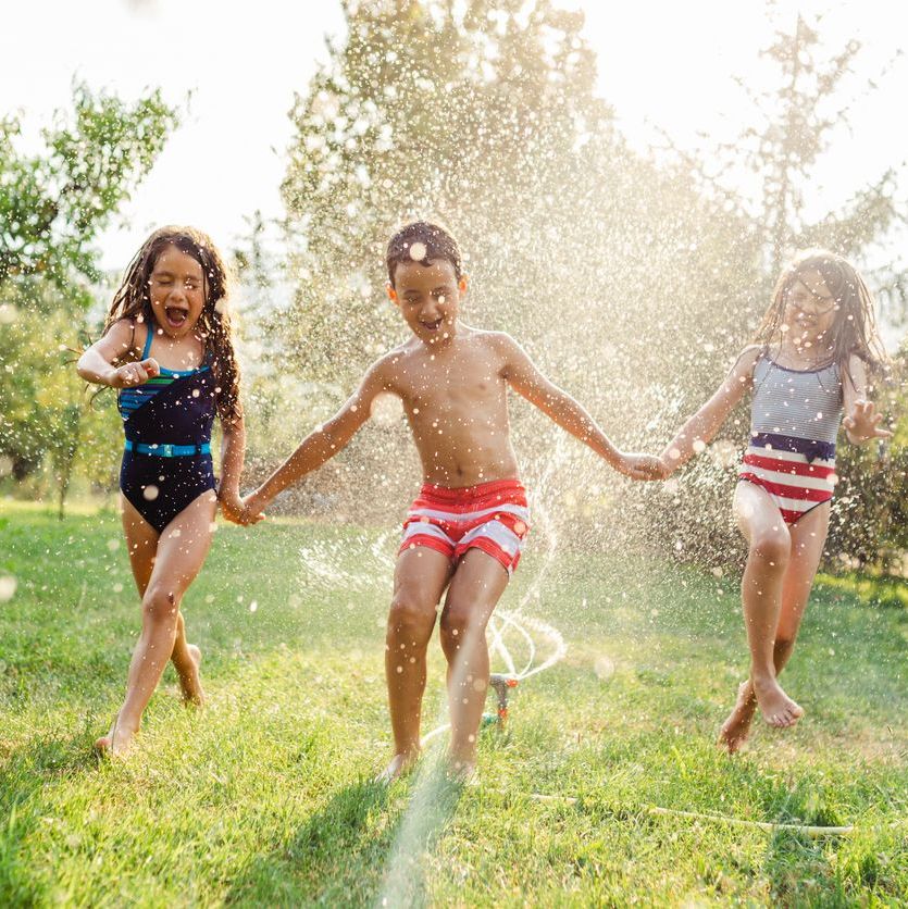 Niños jugando afuera en un día de verano corriendo a través de un aspersor